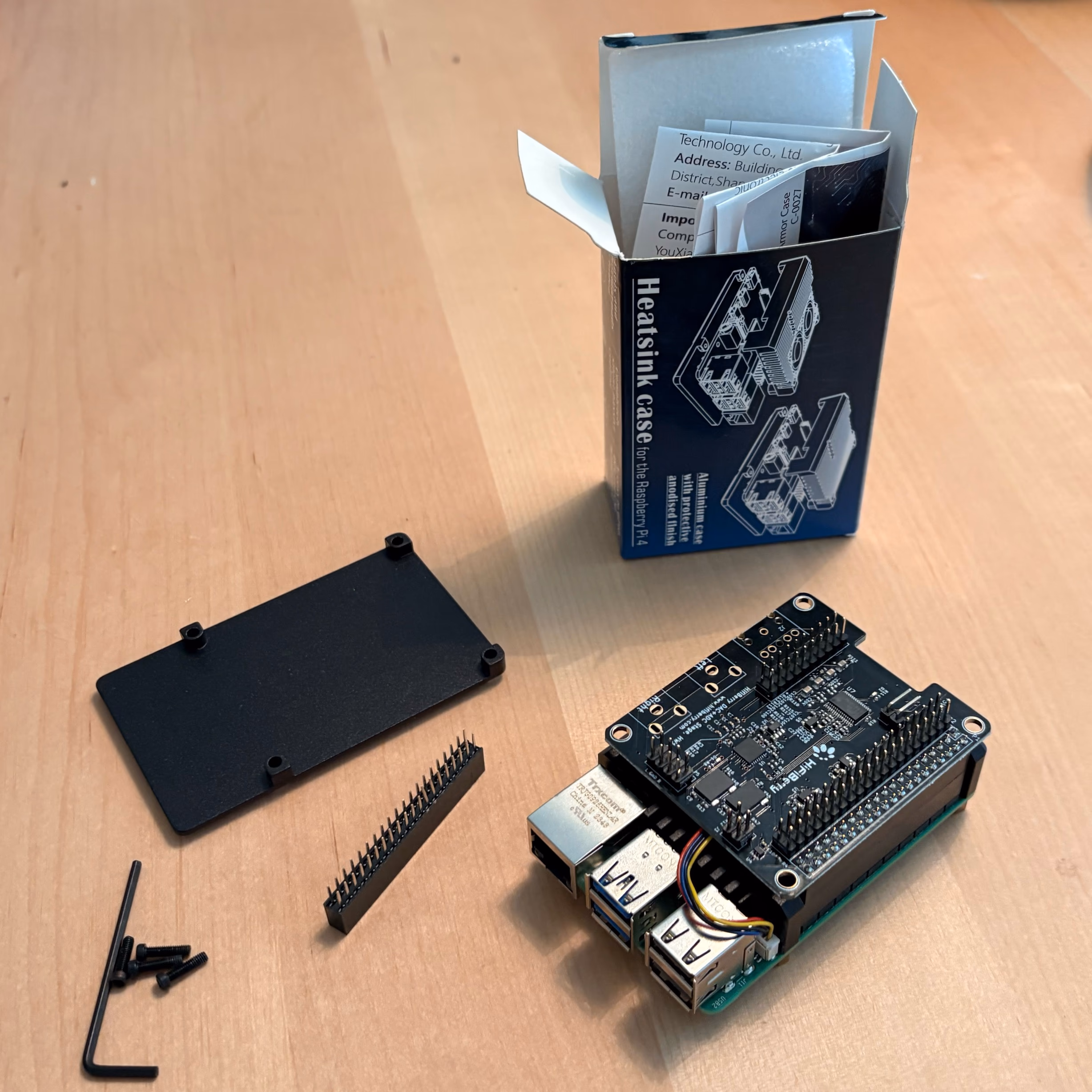 Pi with soundcard seated, next to the heatsink case lid, stacking header, screws and hex key